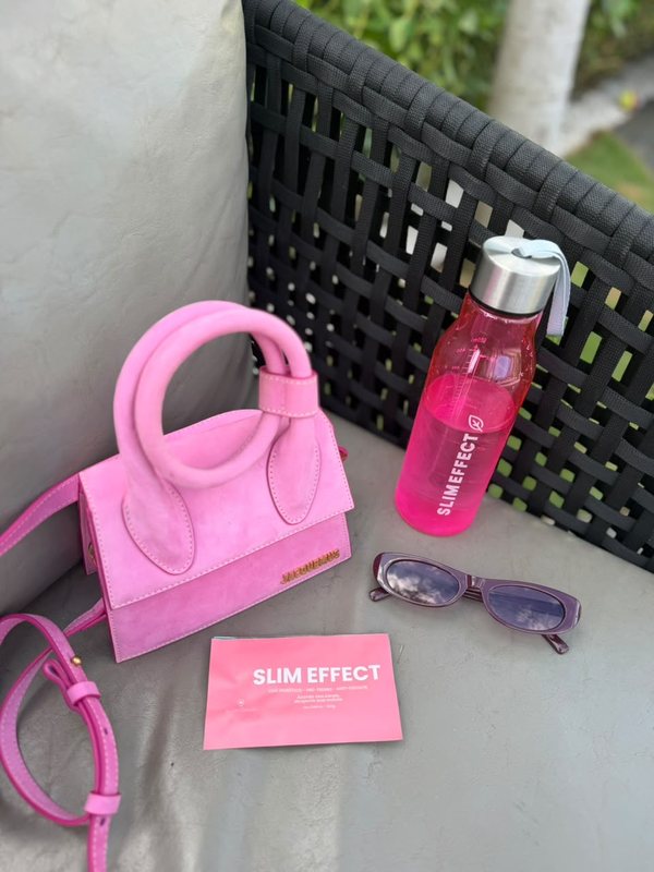 Garrafa personalizada Slim Effect rosa com tampa prata, ao lado de uma bolsa rosa e de um sachê Slim Effect